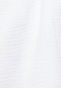 Tissu blanc texturé avec un motif à carreaux subtil, délicatement drapé pour montrer des plis et des ombres douces à la lumière naturelle.