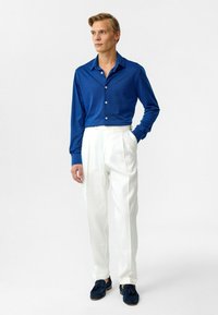 Lange mouw blauwe shirt gemaakt van zachte stof, met knopen; gecombineerd met hoog getailleerde witte broek en marineblauwe instappers. Eenvoudig, schoon ontwerp.