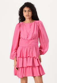Fuchsia rosa klänning med puffade långa ärmar, bältesmidda och lager-på-lager volanger vid fållen. Texturerad tyg ökar det visuella intresset.