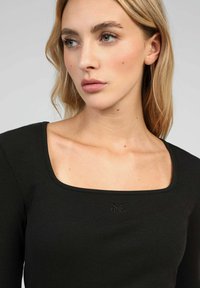 Haut noir à manches longues côtelé avec un décolleté carré et un logo subtil, mettant en valeur une texture lisse et une coupe ajustée.