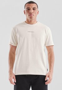 Crème-kleurig t-shirt van zacht, glad weefsel met korte mouwen. Voorzien van een klein, donker logo geborduurd op de borst.
