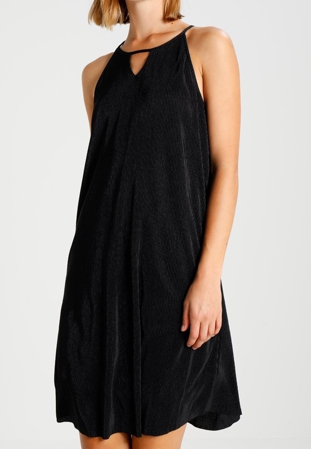 Femme portant une robe noire côtelée sans manches avec un décolleté halter et une petite ouverture en forme de goutte à l’avant.