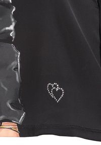 Top negro con un acabado brillante, con un diseño decorativo de corazón de strass en la parte inferior derecha. Textura suave y forma ajustada.