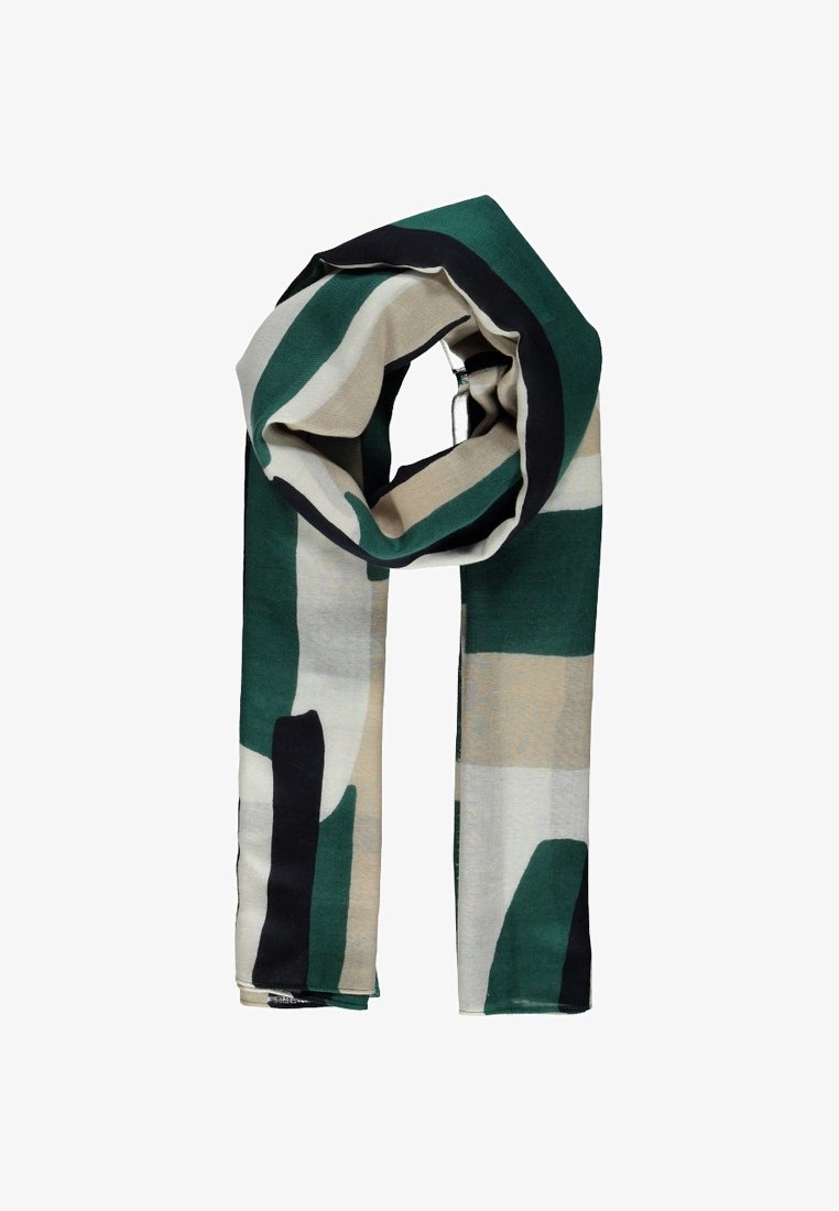 Écharpe avec motifs géométriques abstraits verts, beiges, noirs et blancs, pliée et légèrement bouclée sur un fond blanc.