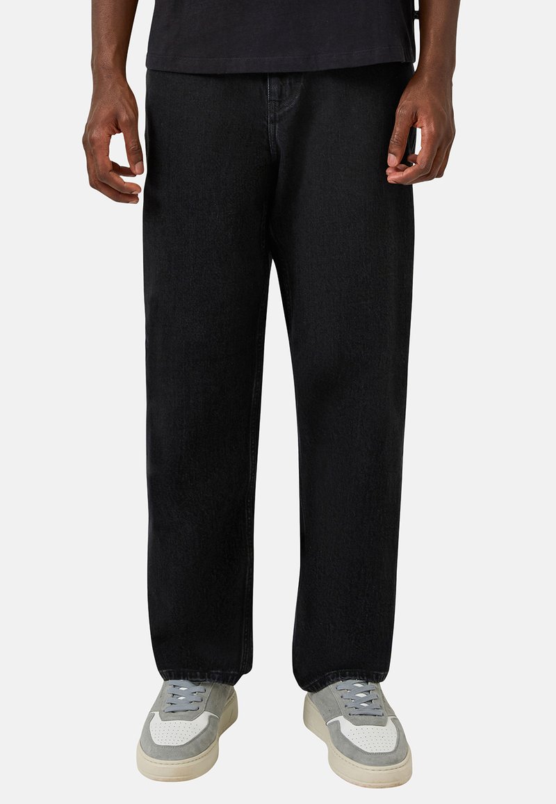 Jean en denim noir ample avec une coupe droite, associé à des baskets gris et blanc avec des lacets et une surface texturée.