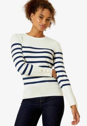 Marineblau- und weiße gestreifte langärmlige Pullover aus weichem Material, mit Rundhalsausschnitt und Knöpfen an den Bündchen. Getragen mit dunklen Jeans.