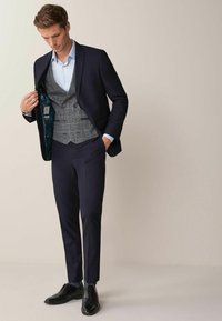 Marinblå kostym med matchande väst, ljusblå skjorta och mönstrade strumpor. Svarta dressade skor fulländar looken. Texturerad västinsida synlig.