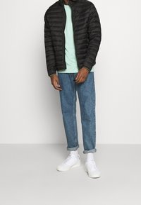 Giacca a vento nera con cuciture orizzontali, t-shirt verde menta, jeans azzurri arrotolati e sneakers bianche. Design semplice e vestibilità casual.