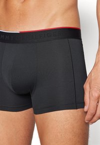 Zwarte boxershorts van rekbaar materiaal met een effen ontwerp. Voorzien van een merkband met witte en rode accenten.