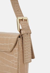 Beige handväska med krokodilstruktur, med ett guldspänne på den justerbara remmen och snygga sömmar.
