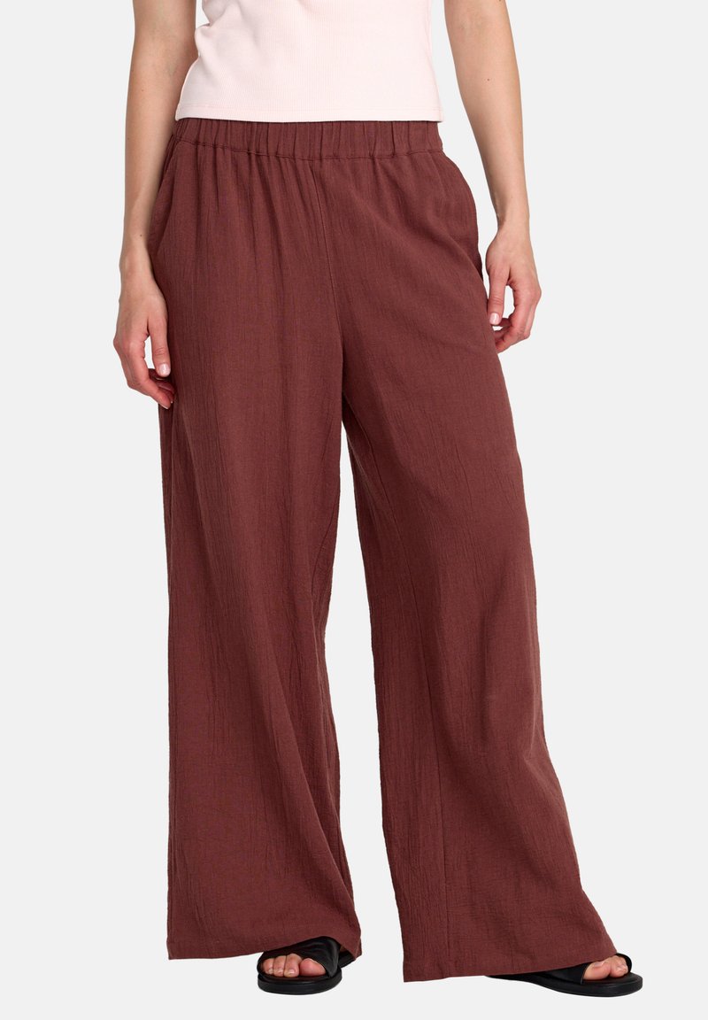 Pantaloni larghi color granata con vita elastica, realizzati in tessuto strutturato, caratterizzati da una vestibilità comoda e tasche laterali. Abbinati a sandali neri.