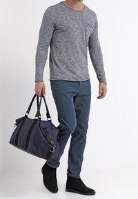 Grijze lange mouw shirt, blauwe broek en zwarte enkellaarsjes. Draagt een marineblauwe sporttas met zwarte straps en zilveren hardware accenten.