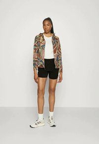 Kamufliažo rašto lengvas švarkas su užtrauktuku priekyje, uždėtas ant baltos palaidinės, derinamas su juodais šortais ir sportiniais bateliais. Lygus audinys, laisvas siluetas.