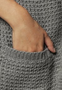 Hand partially inserted into the front pocket of a textured gray knit sweater.