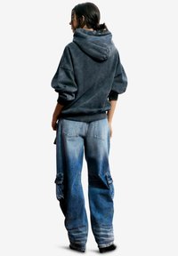 Ciemnoszara, oversize bluza z kapturem, zestawiona z jasnoniebieskimi, dżinsowymi spodniami typu cargo z kieszeniami i efektem gradientu.