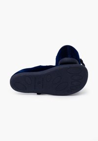 Zapato plano de terciopelo azul con punta redondeada, suela texturizada que presenta patrones de tracción de goma y un tacón bajo para mayor estabilidad.