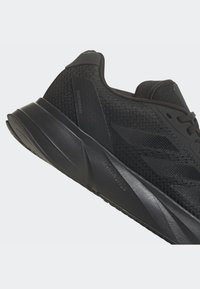 Černá sportovní bota s síťovaným svrškem pro prodyšnost, polstrovanou podrážkou a texturovanými detaily. Na boku a vzadu je logo.