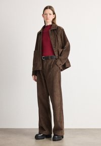 Brown corduroy jacket and matching pants with a textured surface. Red ribbed sweater underneath, black belt, and chunky black boots.