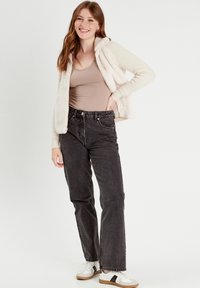 Top sin mangas beige, chaqueta de forro polar crema con cremallera, jeans negros de cintura alta y zapatillas blancas con acentos negros. Texturas suaves, diseño casual.