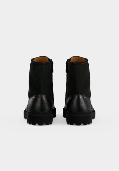 Paire de bottines en cuir noir avec semelles épaisses vues de dos sur un fond clair uni.
