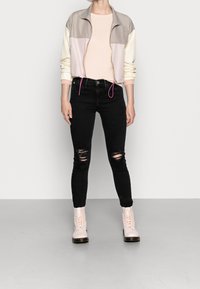 Giubbotto leggero a blocchi di colore con pannelli beige, rosa e crema, abbinato a jeans skinny neri strappati e stivali rosa con lacci.