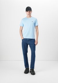 T-shirt en coton bleu clair avec un col rond et un petit logo, associé à un jeans en denim foncé à jambes droites et des baskets noires.