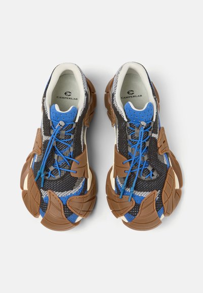 Par de zapatillas CamperLab con parte superior de punto en azul, negro y blanco, suelas gruesas segmentadas en marrón y cordones elásticos azules.