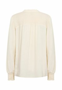 Long-sleeve cream blouse with a textured smocked back panel and gathered cuffs. Soft fabric with a subtle sheen and ruffled neckline.