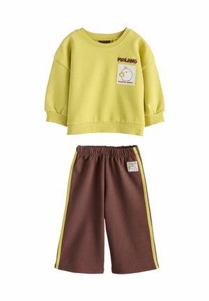 Barn med langt mørkt hår står med ryggen til iført en gul sweatshirt med tegneserie dyr og teksten "Power in kindness better together."