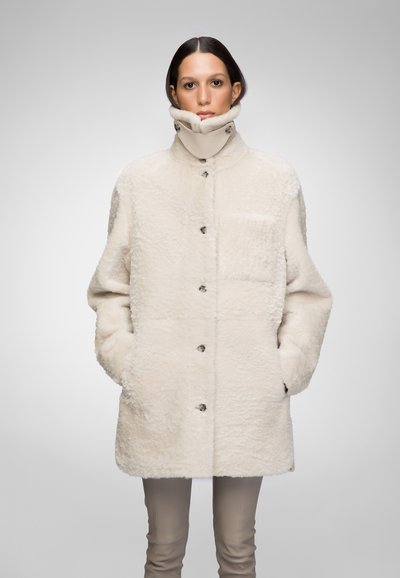 Cappotto in pelliccia finta bianca con colletto alto, caratterizzato da una chiusura frontale con bottoni e una tasca sul petto. Include tasche laterali e un aspetto tessurizzato.