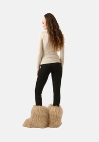 Fény bézs hosszú ujjú felső, fekete leggings és bolyhos bézs csizmavédők texturált felülettel, hátulról, semleges háttér előtt.