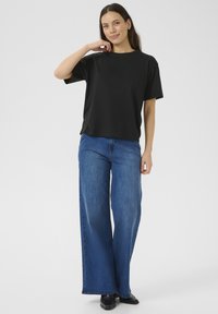T-shirt nera a maniche corte con collo rotondo abbinata a pantaloni in denim blu a gamba larga. L'outfit presenta una vestibilità comoda e un design minimale.