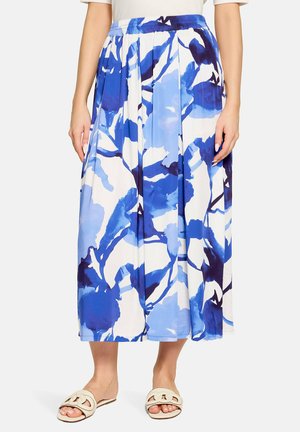 Jupe mi-longue avec imprimé floral abstrait bleu et blanc, portée avec un haut blanc et des sandales beige ouvertes à l'avant, faciles à enfiler.