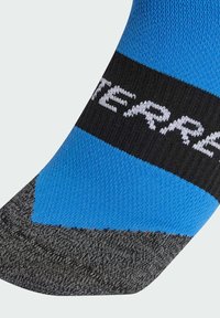 Calcetín deportivo azul y negro con un patrón texturizado, talón reforzado y rayas contrastantes; logotipo mostrado en la banda.