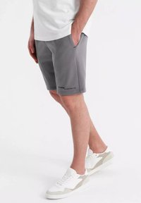 Shorts de sport gris en tissu doux, dotés de poches avant et de détails de couture arrondis. Associés à des baskets blanches avec des accents gris.