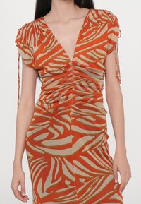 Femme porte une robe cintrée à col en V avec des manches froncées et un motif zébré abstrait orange et beige.