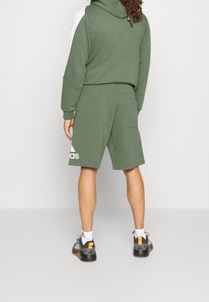 Green cotton hoodie with white accents, paired with matching shorts. Features a kangaroo pocket and logo detail on shorts. Worn with athletic shoes.