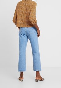 Braune Bluse mit Blumenmuster und Puffärmeln, kombiniert mit hellblauen geraden Jeans und Sandalen im Tiermuster.