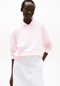 Felpa rosa con collo alto, dotata di branding in rilievo. Abbinata a una gonna bianca, che presenta una vestibilità comoda e una texture morbida.