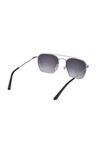 Lunettes de soleil à monture métallique avec des verres carrés à dégradé sombre et des branches fines noires posées ouvertes sur un fond blanc.