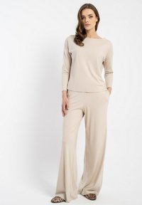 Beżowy zestaw odzieży domowej składający się z bluzki z długim rękawem i szerokim dekoltem oraz luźnych, zwiewnych spodni z szerokimi nogawkami. Miękka, gładka tkanina.
