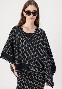Čierny pončo s geometrickým šedým vzorom, dizajn s výstrihom do V, mäkká pletená textura a detail s logom "KARL LAGERFELD" na spodnom leme.
