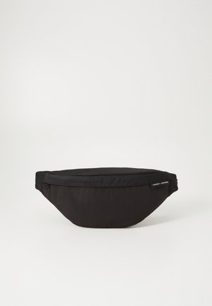 Black fabric waist bag with a streamlined shape, zippered closure, and Tommy Hilfiger branding tag on the side. Soft texture.