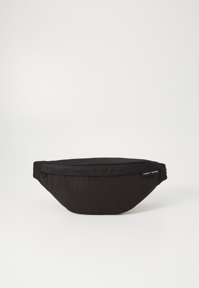 Black fabric waist bag with a streamlined shape, zippered closure, and Tommy Hilfiger branding tag on the side. Soft texture.