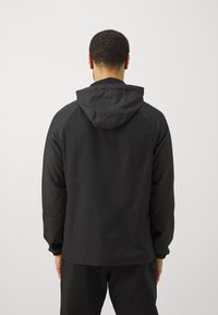 Zwarte hoodie met een gladde textuur, raglanmouwen en elastische boorden, ontworpen voor een casual pasvorm. Achteraanzicht tegen een effen achtergrond.