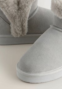 Graue Wildleder-Ankle Boots mit einem weichen, flauschigen Futter und weißen Gummisohlen. Das Design ist schlicht mit einer abgerundeten Zehenpartie und glatter Textur.