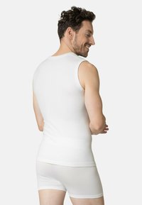 White, sleeveless tank top with a textured pattern, paired with white shorts, showing a fitted design and a smooth, stretchy fabric.