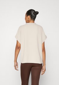 Ljusbeige kortärmad topp med lös passform. Mjuk textur, rundad halsringning och uppvikta ärmar i kombination med bruna räfflade byxor.