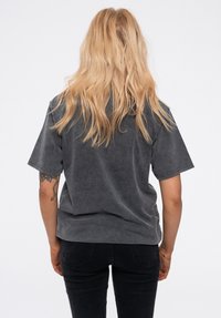 Gray short-sleeve T-shirt in a soft, textured fabric, features a relaxed fit and is paired with black jeans. No visible branding or patterns.