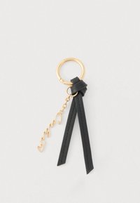 Porte-clés Calvin Klein doré avec boucle en cuir noir et pendentif en script doré suspendu à une chaîne sur fond blanc.